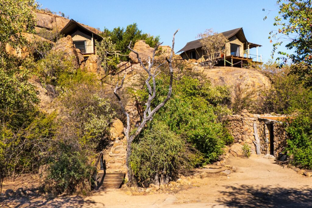 Rustic safari lodges surrounded by rocky landscape and desert vegetation, perfect for an adventurous retreat.